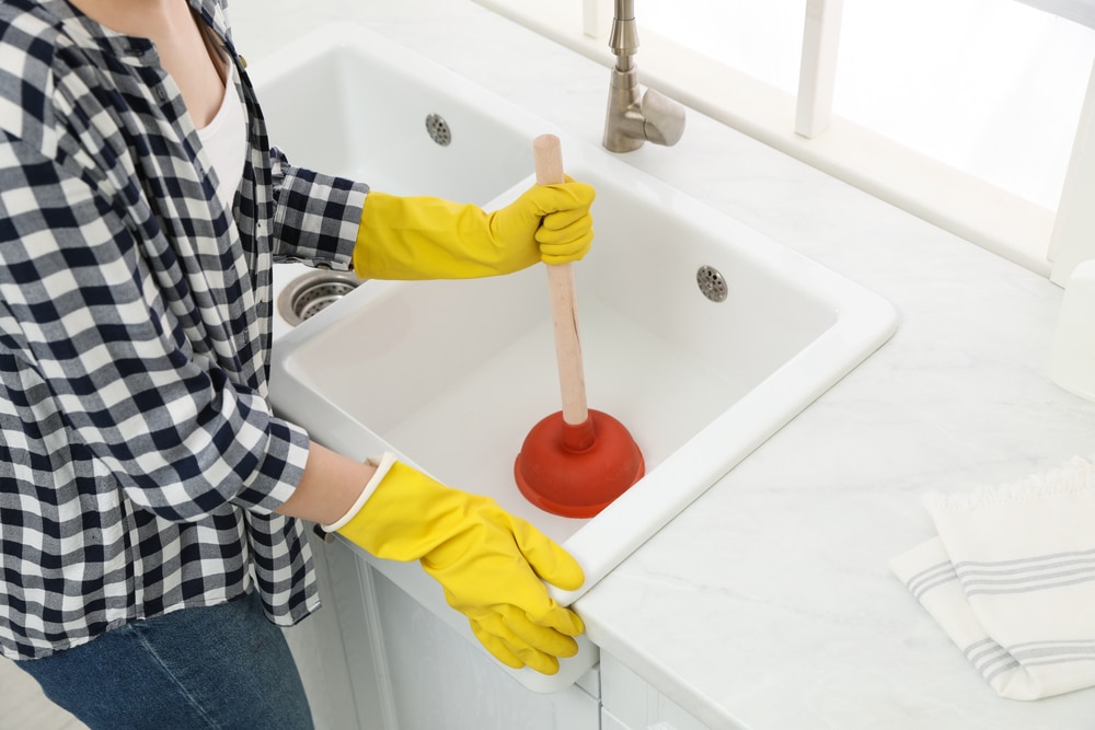 Woman,Using,Plunger,To,Unclog,Sink,Drain,In,Kitchen,,Closeup